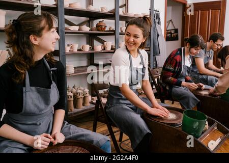 Begeisterte Menschen in Schürzen arbeiten mit Ton Bildhauerei auf Töpferscheibe mit Hilfe von Handwerkern in großen Licht-Werkstatt Stockfoto