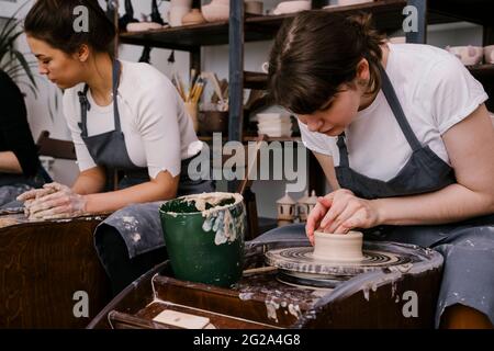 Begeisterte Menschen in Schürzen arbeiten mit Ton Bildhauerei auf Töpferscheibe mit Hilfe von Handwerkern in großen Licht-Werkstatt Stockfoto