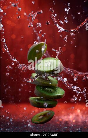 Spritzer in Scheiben geschnittener Kiwi mit Wassertropfen auf rotem Hintergrund Stockfoto