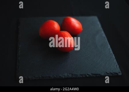 Eine Gruppe Tomaten liegt auf einem schwarzen Servierbrett in der Mitte Stockfoto