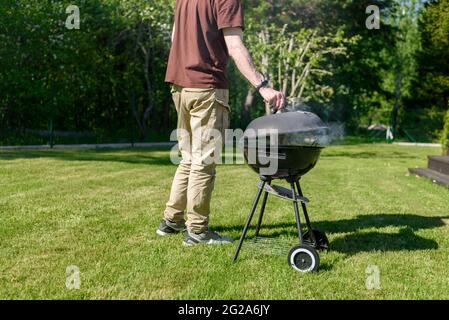 Mann, der Grillfleisch am sonnigen Sommertag auf dem Hinterhof zubereitet Stockfoto