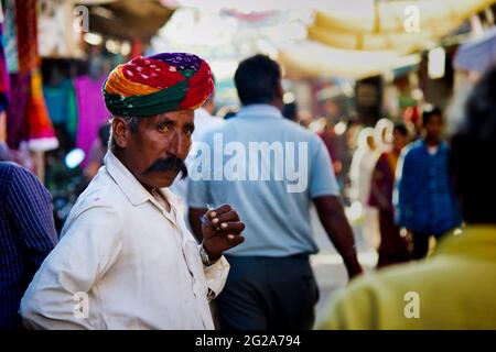 Pushkar, Indien - 10. NOVEMBER 2016: Ein alter Rajasthani-Mann in traditioneller ethnischer Kleidung wie buntem Turban und typischer weißer Hemdraucherzigarette Stockfoto