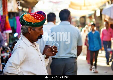 Pushkar, Indien - 10. NOVEMBER 2016: Ein alter Rajasthani-Mann in traditioneller ethnischer Kleidung wie buntem Turban und typischer weißer Hemdraucherzigarette Stockfoto