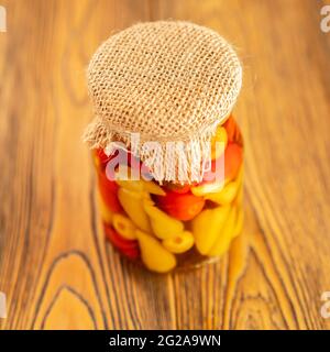 Eingelegter Pfeffer in einem Glas. Hausgemachte Zubereitungen auf rustikale Weise. Ein würziger Snack. Gebunden mit Jute-Faden. Rustikaler Stil. Selektiver Fokus. Stockfoto