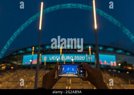 Wembley Stadium, Wembley Park, Großbritannien. Juni 2021. Frau, die vor dem Start der Euro 2020 ein beleuchtetes Wembley-Stadion auf ihrem Mobiltelefon fotografiert. Die UEFA-Fußballeuropameisterschaft beginnt am 11. Juni 2021 und wird um ein Jahr verschoben, als die Coronavirus-Pandemie 2020 weltweit eintraf. Am 13. Juni 2021 findet im Wembley-Stadion das erste Spiel, England gegen Kroatien, statt. Amanda Rose/Alamy Live News Stockfoto