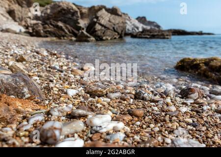 Marmorsteine aus nächster Nähe am wilden kiesstrand des mittelmeers mit felsigen Klippen und blauem klarem Wasser. Reisen Sie nach Griechenland in der Nähe von Athen. Sommer Natur s Stockfoto