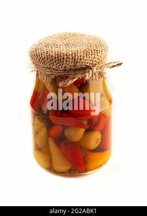 Eingelegter Pfeffer in einem Glas. Isoliert auf weißem Hintergrund. Ein würziger Snack. Gebunden mit Jute-Faden. Rustikaler Stil. Selektiver Fokus. Stockfoto