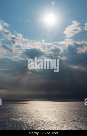 Sonnenstrahlen, die durch Wolken über dem Meer in Griechenland scheinen. Dramatische Wolkenlandschaft auf der wasseroberfläche des mittelmeers. Vertikal Stockfoto