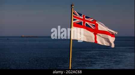 Die Flagge der britischen Royal Navy The White Ensign, die vom Fähnrich-Stab eines britischen Kriegsschiffs geflogen wird Stockfoto