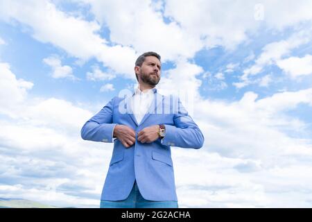 Schöner reifer Mann Geschäftsmann in Anzug Check-Zeit auf Armbanduhr auf Himmel Hintergrund, formalwear. Stockfoto