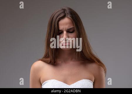 Schwül-petulant Attraktive junge Frau, die ihre Lippen in einem Nahaufnahme-Porträt mit Kopf und Schultern auf grauem Studiohintergrund schlingt und ausschüttet Stockfoto