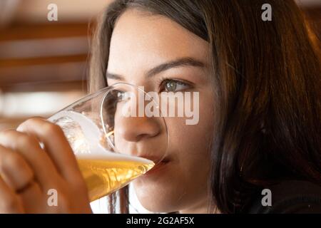 Gesicht einer schönen jungen Frau mit langen Haaren, die ein Glas Bier hält und trinkt, Nahaufnahme von Details, Studio und Getränken Stockfoto