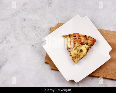 Frittata mit Kartoffeln, grünen Erbsen, Käse und Wurst auf einem weißen rechteckigen Teller serviert auf einem hölzernen Schneidebrett auf einem hellgrauen Hintergrund. Stockfoto