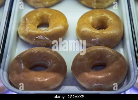 Ein Tablett voll mit leckeren glasierten Donuts, die auf einem Regal in einem Vitrinen aus Glas platziert sind. Selektiver Fokus. Stockfoto