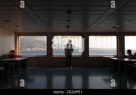 Messina-Straße, Italien - 05. Juli 2010: Rückansicht eines Mannes, der vom großen Fenster der Fähre aus die Küste betrat, andere Passagiere sitzen ich Stockfoto