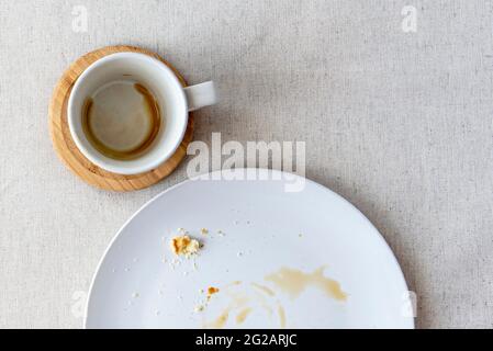 Tisch mit Tischdecke bedeckt mit Kaffeebecher für Espresso, Teller mit Krümel von Dessert, Draufsicht, flaches Lay Stockfoto