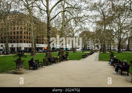 London, Großbritannien - 21. April 2021: Menschen, die an einem kühlen Frühlingsnachmittag die öffentlichen Bänke auf dem berühmten Berkeley Square in Mayfair, London genießen. Stockfoto