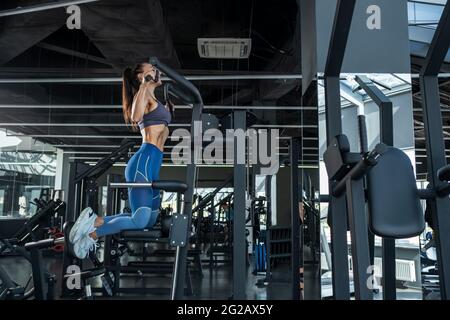 Konzentriertes athletisches Mädchen, das im Fitnessstudio an der Maschine hochzieht Stockfoto