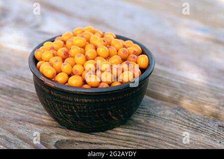 Frische orange Sanddornbeeren in brauner Schale auf Holzgrund. Sommer-Frühstück außerhalb auf dem Land. Stockfoto