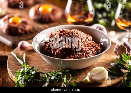 Weiße Schüssel mit rohem Fleisch gefüllt, bereit, köstliche Steak Tartare mit herzhaften Eigelb zuzubereiten. Bereits vorbereitete Tartares im Hintergrund mit Rum und Stockfoto