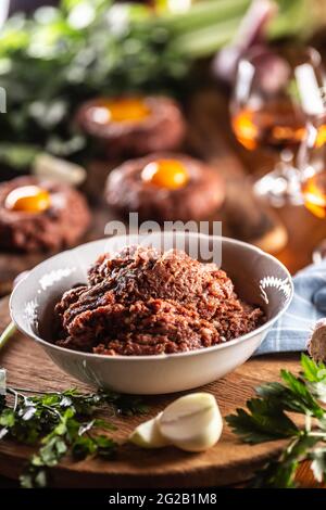 Weiße Schüssel mit rohem Fleisch gefüllt, bereit, köstliche Steak Tartare mit herzhaften Eigelb zuzubereiten. Bereits vorbereitete Tartares im Hintergrund mit Rum und Stockfoto