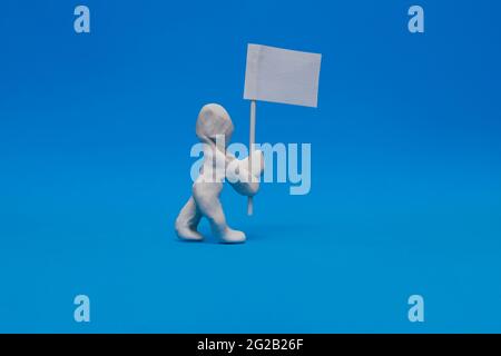 Ein weißer Plastikdummy mit einer weißen Flagge auf blauem Hintergrund. Der Dummy hält den Fahnenmast, der in Weiß gehalten ist, so dass er personalisiert werden kann. Stockfoto