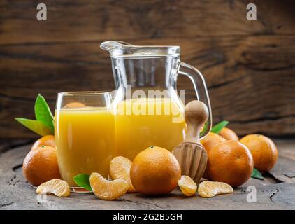 Orangefarbene Mandarinenfrüchte und frischer Mandarinensaft auf dunklem Holzhintergrund. Stockfoto