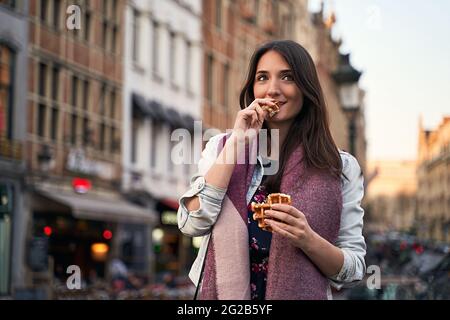 Fröhliches Mädchen, das auf der City Street spazieren ging und belgische Waffeln isst Stockfoto