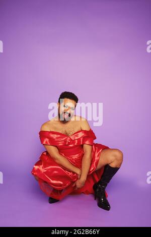 Porträt einer Drag Queen posiert auf violettem Hintergrund. Gender Queer im Theateroutfit lächelt im Studio. Stockfoto