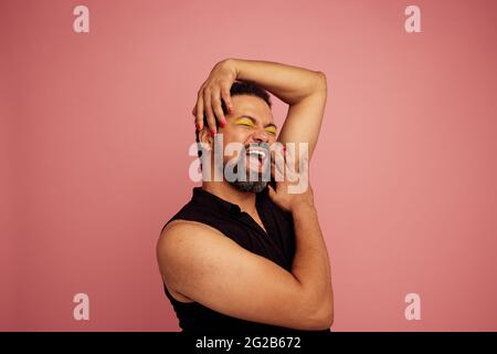 Selbstbewusster und ausdrucksstarker Mann auf rosa Hintergrund. Ziehen Sie die Königin in Make-up und lächeln Sie. Stockfoto