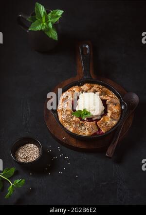Hausgemachter Galette-Kuchen mit Erdbeeren, Vanilleeis und Sesam im dunklen rustikalen Stil. Stockfoto