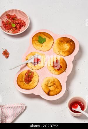 Hausgemachte Mini-Käsekuchen mit rosa Johannisbeer-Fruchtaufstrich und Beeren in einer Keramik-Muffin-Pfanne. Speicherplatz kopieren. Stockfoto