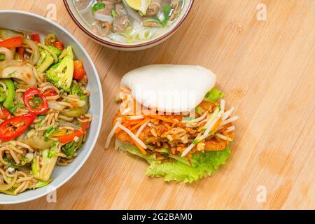 Asiatische Speisen zum Mitnehmen auf Holztisch. Pho Suppe, bao Bun, Meeresfrüchte Nudeln Gerichte nach Hause liefern Stockfoto