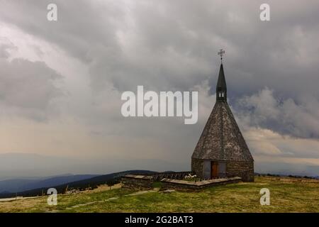 Kleine Kapelle mit Regenwolken auf dem Gipfel von einem Berg beim Wandern Stockfoto