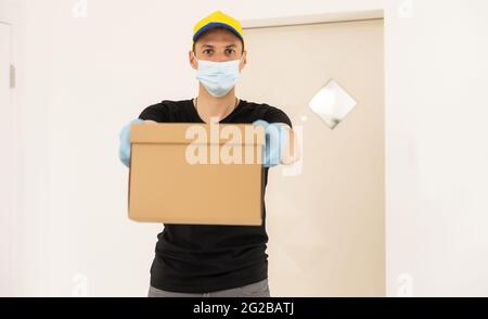 Lieferer hält Kartons in medizinischen Gummihandschuhen und Maske. Platz kopieren. Schnelle und kostenlose Lieferung. Online-Shopping und Express-Lieferung Stockfoto