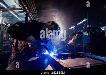 Die beiden Handwerker beim Schweißen und Schleifen an ihrem Arbeitsplatz in der Werkstatt, während die Funken um sie herum "fliegen", tragen sie einen schützenden HE Stockfoto