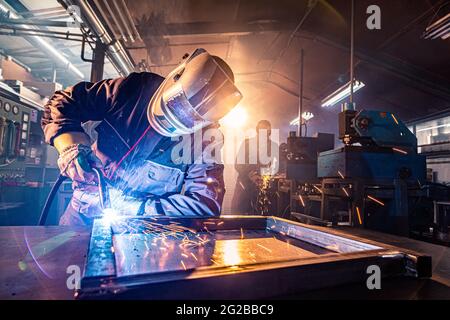 Die beiden Handwerker beim Schweißen und Schleifen an ihrem Arbeitsplatz in der Werkstatt, während die Funken um sie herum "fliegen", tragen sie einen schützenden HE Stockfoto