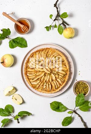 Blick von oben auf frisch gebackene Apfelkuchen-Torte mit Pudding-Füllung und grünen Pistazien auf hellem Stein-Hintergrund. Stockfoto