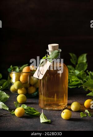 Eine Glasflasche mit köstlichem gelben Pflaumenlikör oder Wein auf einem Holztisch. Hausgemachtes starkes alkoholisches Getränk. Stockfoto