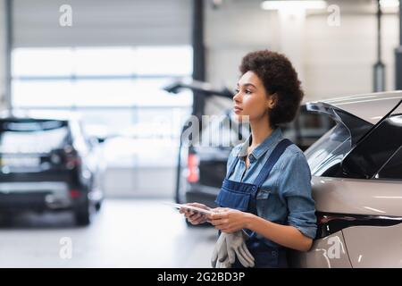Junger afroamerikanischer Mechaniker, der mit digitaler Tablette in der Nähe des Autos im Autoreparaturdienst steht Stockfoto