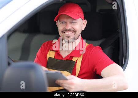 Lächelndes Porträt eines männlichen Kurierfahrers, der Dokumente im Autofenster hält Stockfoto