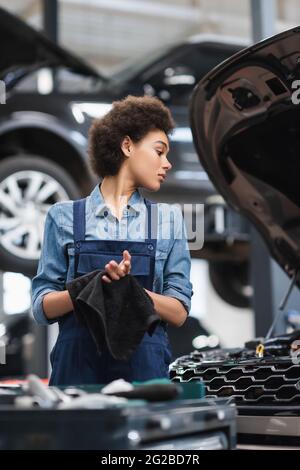 Junger afroamerikanischer Mechaniker in Overalls, der in der Garage die Hände mit einem Handtuch trocknete Stockfoto