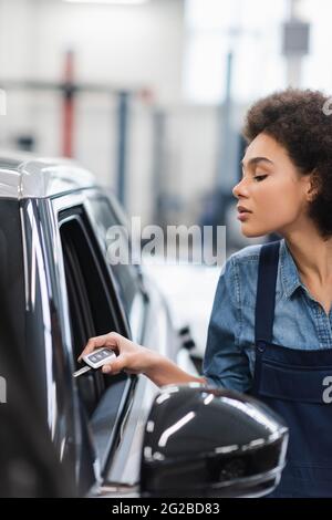 Junger afroamerikanischer Mechaniker in Overalls mit Schlüssel in der Nähe des Autos in der Garage Stockfoto