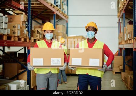 Diverse Arbeiter in Masken, die Kisten im Lager tragen Stockfoto