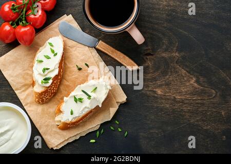 Sandwich mit Weichkäse mit grünen Zwiebeln und Brot auf dunklem Holzboden. Einfaches Frühstück mit Ricotta-Sandwich und Kaffee. Kopierer in der Draufsicht Stockfoto