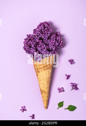 Kreatives Stillleben eines Eiswaffelkegels mit Fliederblüte auf rosa Hintergrund. Draufsicht. Stockfoto