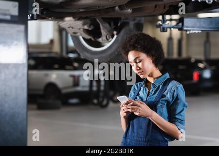Junger afroamerikanischer Mechaniker hält Handy in der Garage in den Händen Stockfoto
