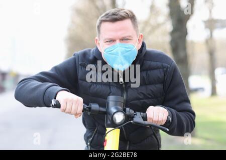 Mann in medizinischer Schutzmaske fährt Elektroroller um die Stadt Stockfoto