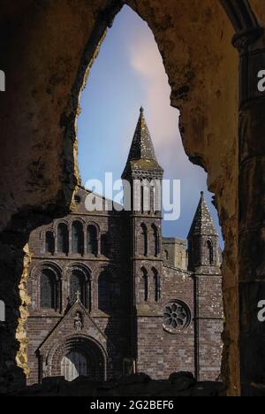 Ein spitzes gotisches Fenster in der Ruine des Bischofspalastes aus dem 14. Jahrhundert neben der St Davids Cathedral in Pembrokeshire, Wales, Großbritannien, umrahmt einen Turm und einen Teil der Kathedrale an der Westfront, 1793 in lila Sandsteinen in gemischten Stilen und nach schlechten technischen Standards umgebaut vom gefeierten neoklassizistischen Architekten Regency und Georgien, John Nash, Designer des Londoner Buckingham Palace, Marble Arch und Regent Street und Brighton's Royal Pavilion. Die Fassade musste in den 1860er Jahren umgestaltet werden, als sie sich nach außen neigte und in den 1990er Jahren weitere größere Reparaturen erforderlich machte. Stockfoto