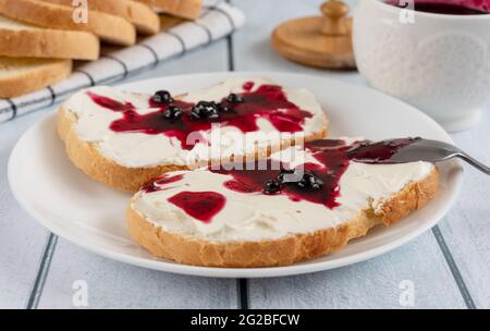 Geröstetes Brot mit Frischkäse und Heidelbeermarmelade auf einem Holztisch Stockfoto